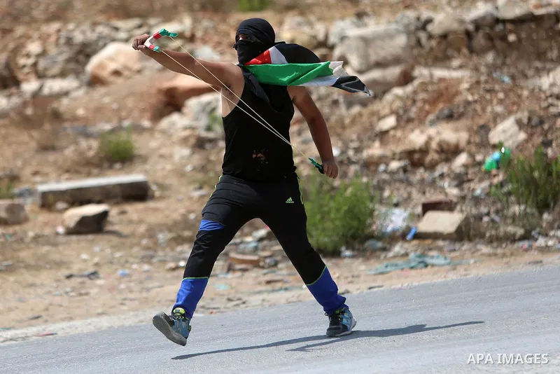 A Palestinian protester uses a slingshot to hurl stones towards Israeli troops during clashes following a protest in solidarity with Palestinian prisoners held in Israeli jails, near Israel's Ofer Prison near the West Ba...