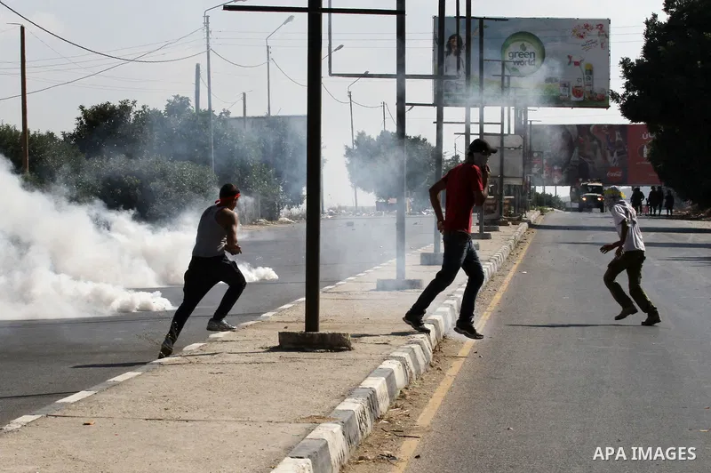 Palestinian protesters run for cover from a tear gas canister fired by Israeli troops during clashes following a protest in solidarity with Palestinian prisoners held in Israeli jails, at the Hawara checkpoint near the W...