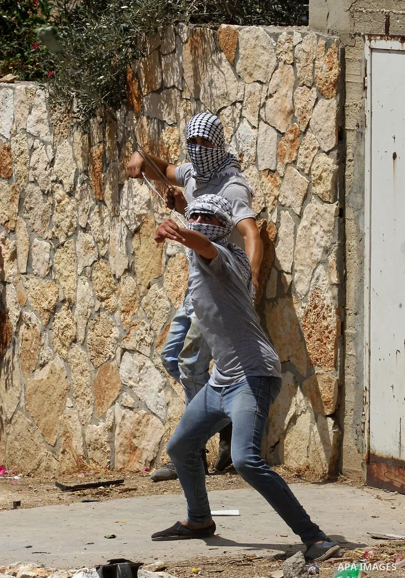 Palestinian protesters use a slingshot to hurl stones towards Israeli security forces during clashes following a weekly demonstration against the expropriation of Palestinian land by Israel on August 19, 2016, in the vil...