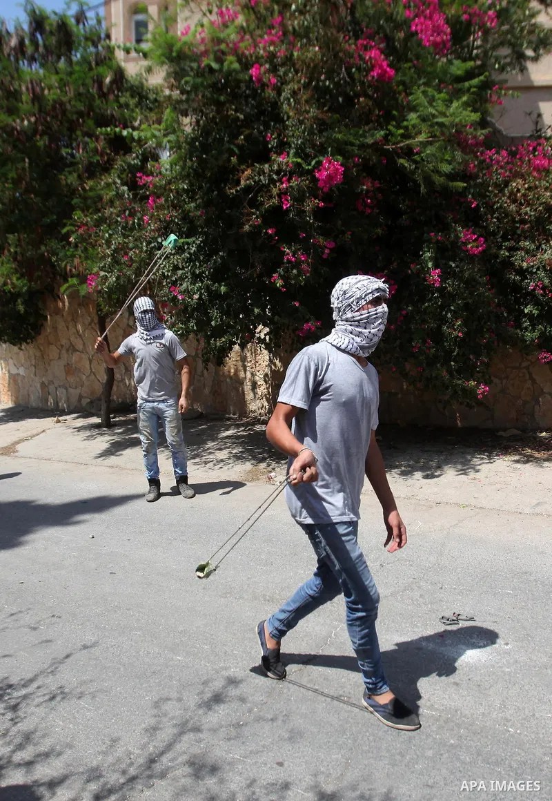 Palestinian protesters use a slingshot to hurl stones towards Israeli security forces during clashes following a weekly demonstration against the expropriation of Palestinian land by Israel on August 19, 2016, in the vil...