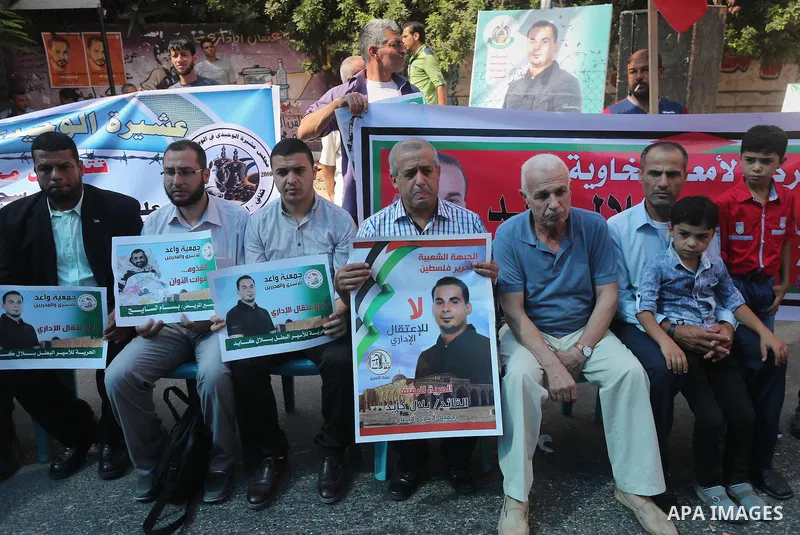 Palestinians hold posters against administrative detention and in support of Palestinian prisoner Bilal Kayed (portrait), who has been fasting for almost two months over his detention without trial, in front of Red Cross...