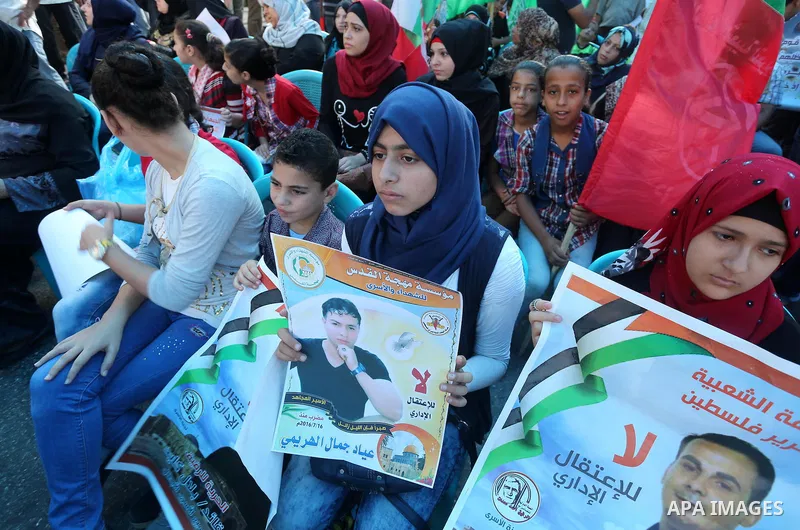 Palestinians hold posters against administrative detention and in support of Palestinian prisoner Bilal Kayed (portrait), who has been fasting for almost two months over his detention without trial, in front of Red Cross...