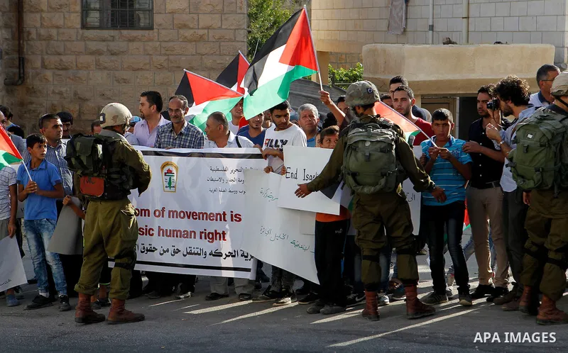 Palestinian demonstrators hold signs in front of Israeli soldiers during a protest calling for the reopening of a closed street in the West Bank city of Hebron August 24, 2016. Photo by Wisam Hashlamoun