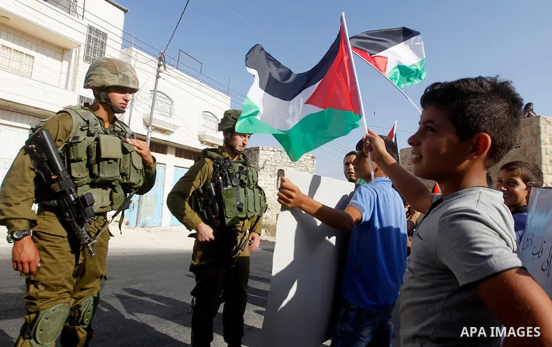 Palestinian demonstrators hold signs in front of Israeli soldiers during a protest calling for the reopening of a closed street in the West Bank city of Hebron August 24, 2016. Photo by Wisam Hashlamoun
