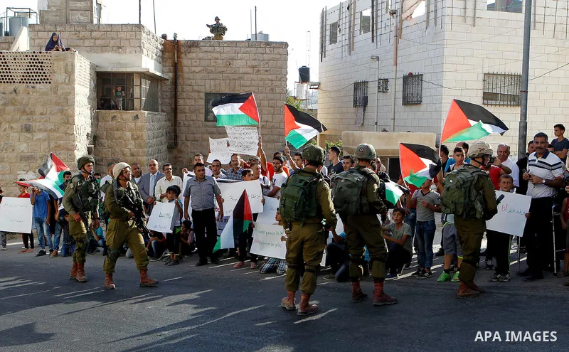 Palestinian demonstrators hold signs in front of Israeli soldiers during a protest calling for the reopening of a closed street in the West Bank city of Hebron August 24, 2016. Photo by Wisam Hashlamoun
