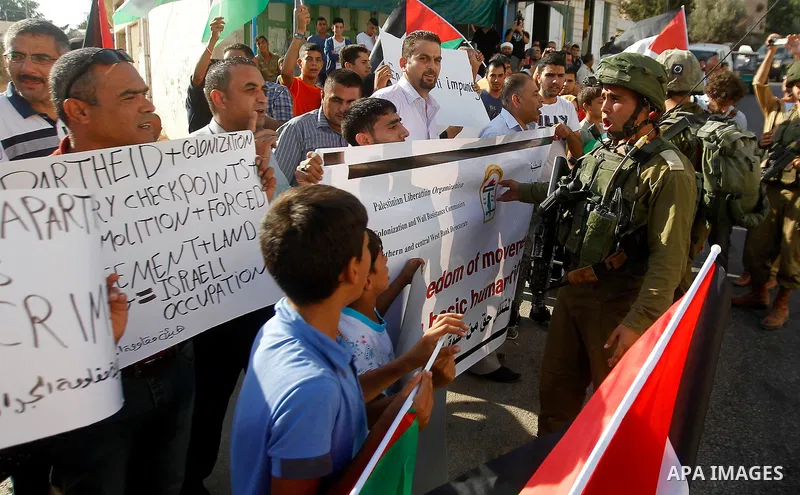 Palestinian demonstrators hold signs in front of Israeli soldiers during a protest calling for the reopening of a closed street in the West Bank city of Hebron August 24, 2016. Photo by Wisam Hashlamoun