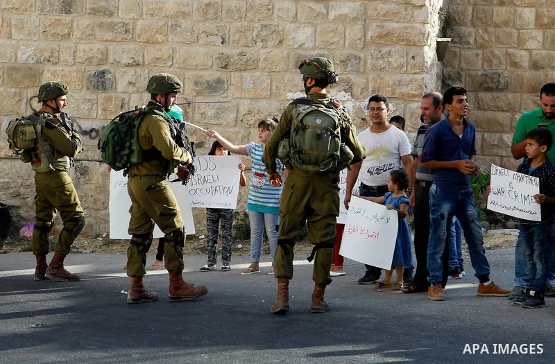 Palestinian demonstrators hold signs in front of Israeli soldiers during a protest calling for the reopening of a closed street in the West Bank city of Hebron August 24, 2016. Photo by Wisam Hashlamoun
