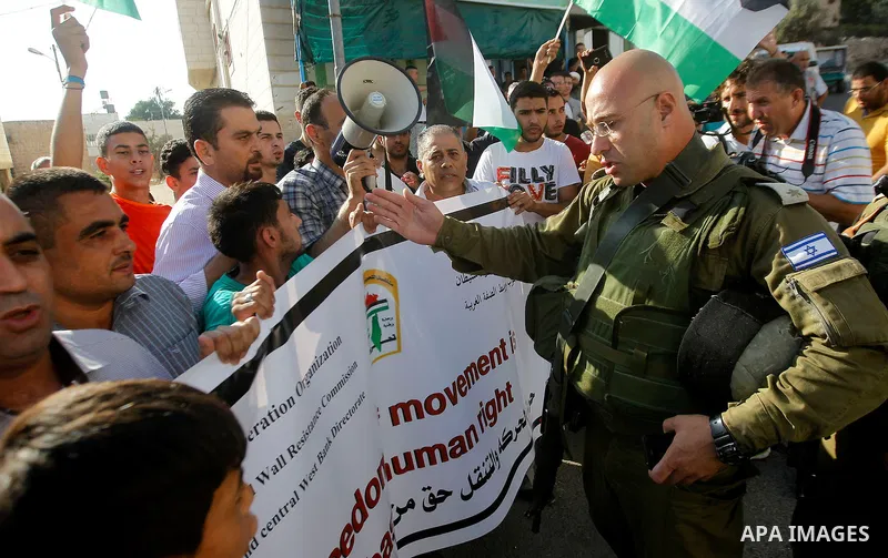 Palestinian demonstrators hold signs in front of Israeli soldiers during a protest calling for the reopening of a closed street in the West Bank city of Hebron August 24, 2016. Photo by Wisam Hashlamoun