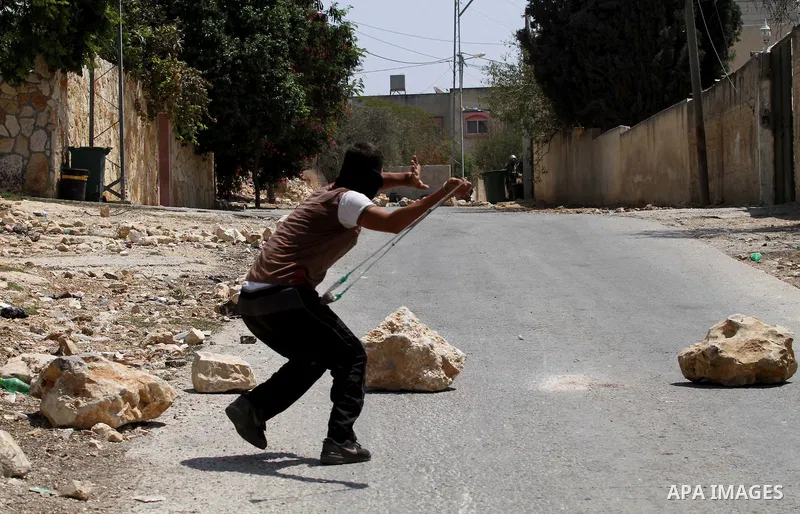 A Palestinian protester uses a slingshot to hurl stones towards Israeli security forces during clashes following a weekly demonstration against the expropriation of Palestinian land by Israel on August 26, 2016, in the v...