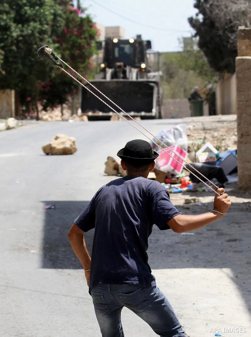 A Palestinian protester uses a slingshot to hurl stones towards Israeli security forces during clashes following a weekly demonstration against the expropriation of Palestinian land by Israel on August 26, 2016, in the v...
