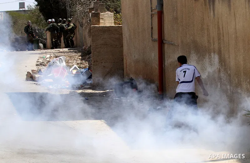 A Palestinian protester takes cover from a tear gas canister fired by Israeli security forces during clashes following a weekly demonstration against the expropriation of Palestinian land by Israel on August 26, 2016, in...