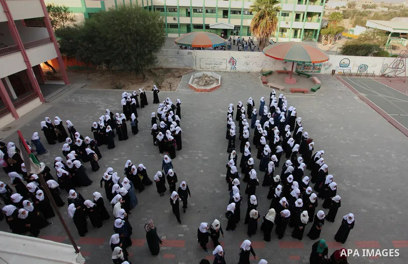 Palestinian schoolgirls play exercises inside their school in the morning of the first day of the new year study in Khan Younis in the southern Gaza Strip August 28, 2016. The mural reads. Photo by Ashraf Amra