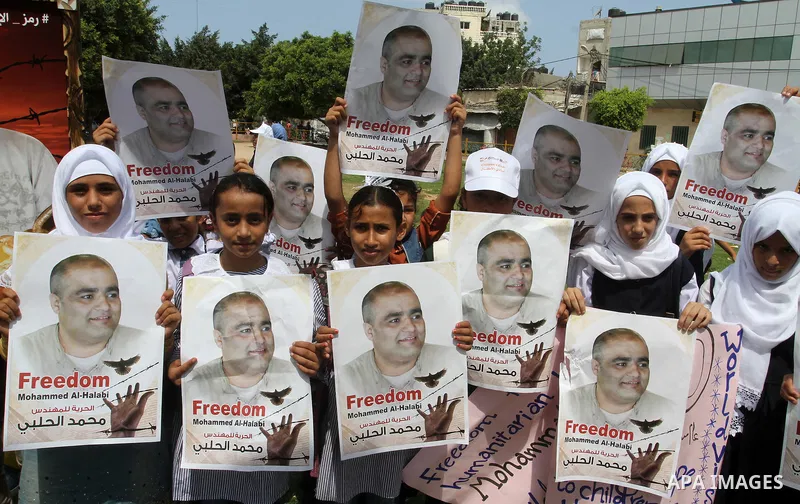 Palestinian demonstrators hold posters of Mohammad El Halabi, World Vision's manager of operations in Gaza who was accused by Israel of funnelling millions of dollars in aid money to Hamas, during a protest in solidarity...
