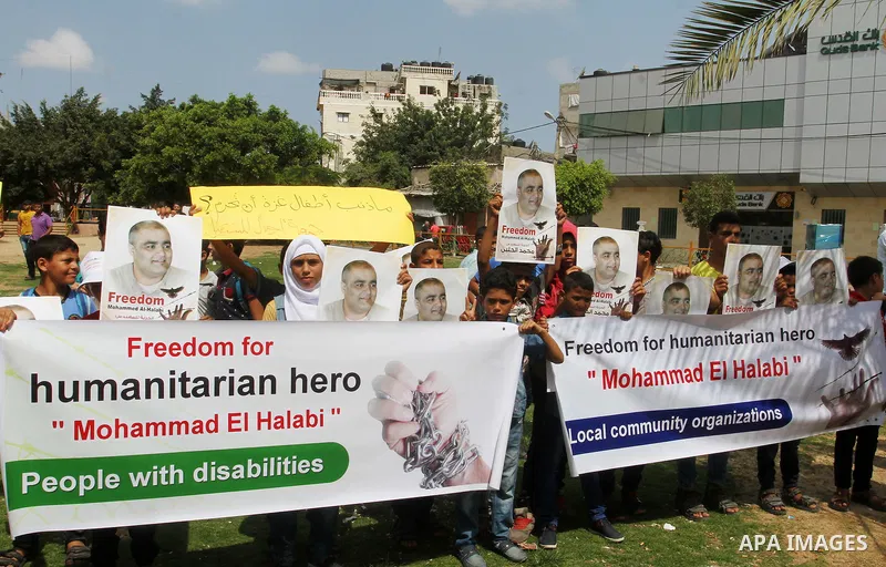 Palestinian demonstrators hold posters of Mohammad El Halabi, World Vision's manager of operations in Gaza who was accused by Israel of funnelling millions of dollars in aid money to Hamas, during a protest in solidarity...