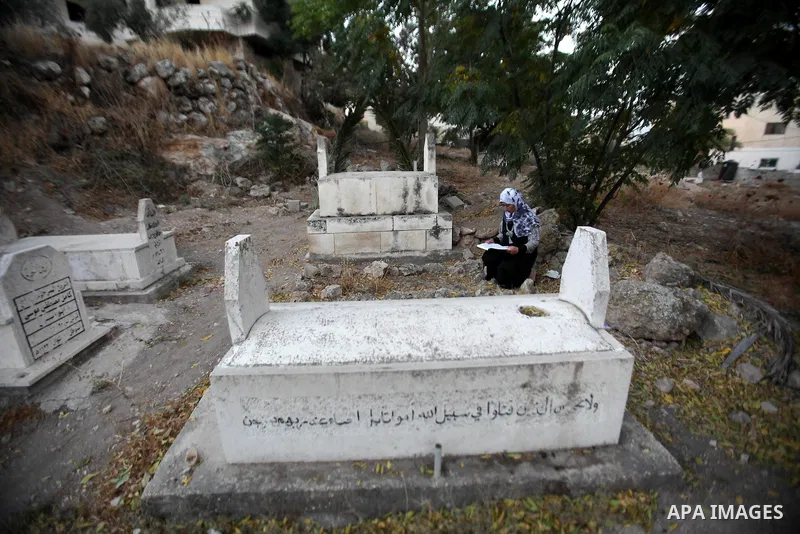 A Palestinian woman reads the Koran next to the grave of her relative at a cemetery on the first day of Eid al-Adha, or feast of the sacrifice, in the West Bank city of Nablus, on Sep. 12, 2016. Muslims around the world...