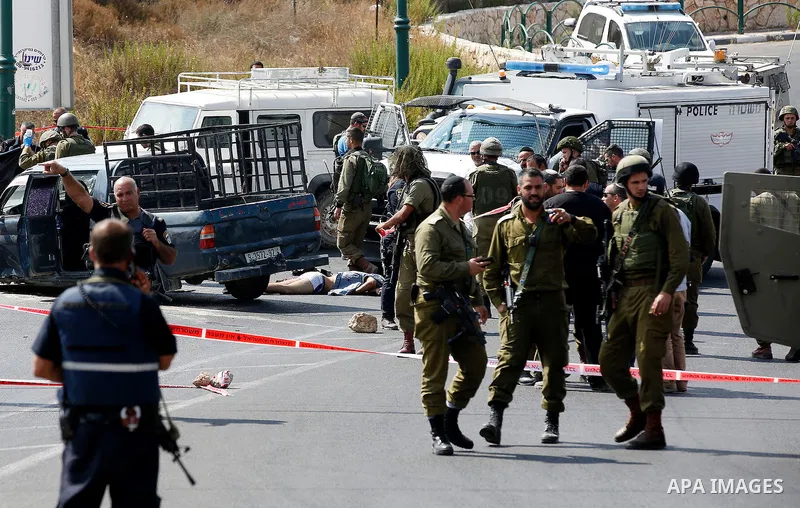Israeli security forces gather around the body of Palestinian Fares Khadour, whom the Israeli military said was shot dead by Israeli forces after he rammed a car into a bus stop near the Jewish settlement of Kiryat Arba...
