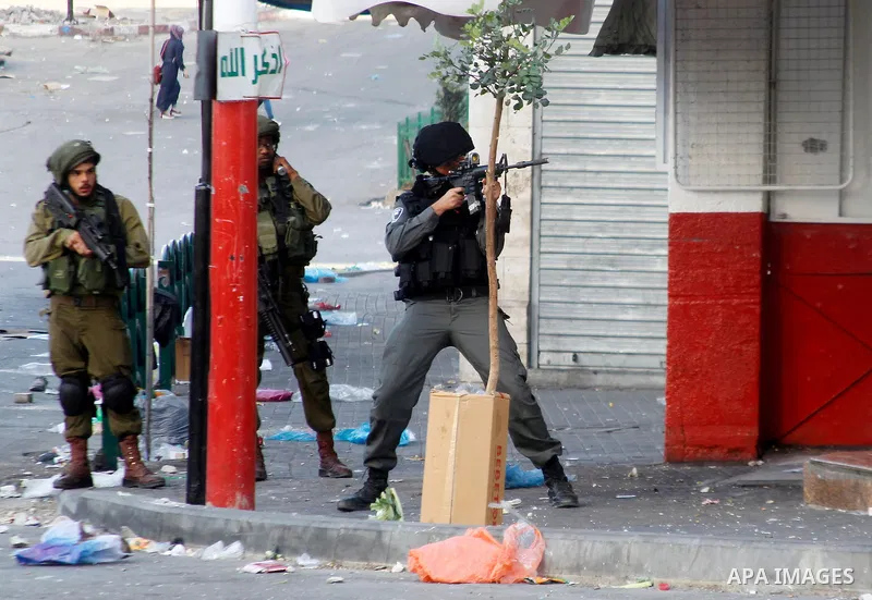 A member of Israeli security forces aims his weapon towards Palestinian protesters during clashes following two Palestinians were shot dead during a stabbing attack against Israeli border police in the West Bank city of...