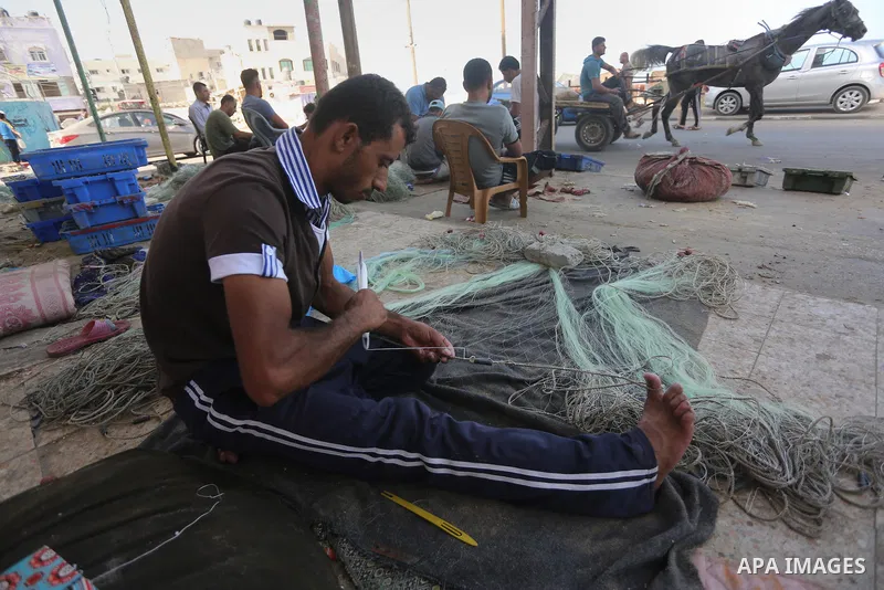 A Palestinian fisherman fixes a fishing net, at the beach in Gaza City, on Sept. 21, 2016. Photo by Mohammed Asad