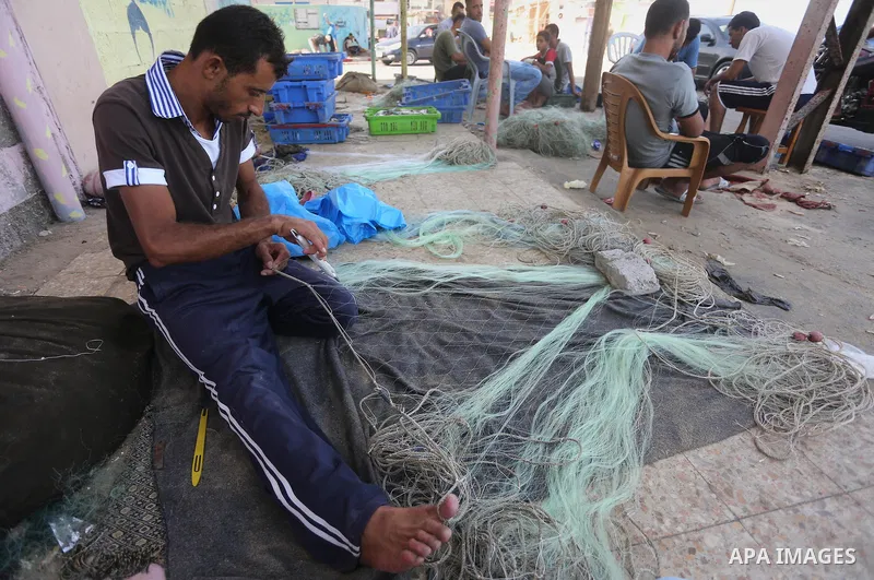 A Palestinian fisherman fixes a fishing net, at the beach in Gaza City, on Sept. 21, 2016. Photo by Mohammed Asad