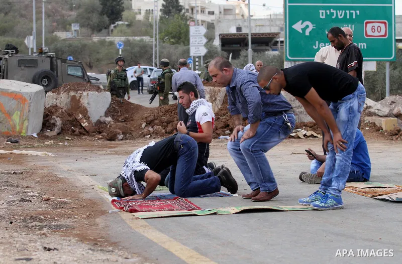 Palestinians perform Friday prayers, as Israeli soldiers look on, next to the Beta Junction east West Bank city of Nablus, on September 23, 2016, to protest against the closure of the entrance of the Beta village by the...