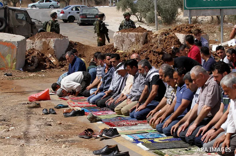 Palestinians perform Friday prayers, as Israeli soldiers look on, next to the Beta Junction east West Bank city of Nablus, on September 23, 2016, to protest against the closure of the entrance of the Beta village by the...