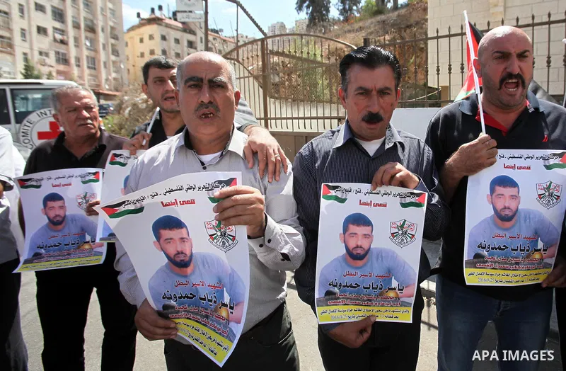 Palestinians hold pictures of Yassir Hamduni, who died of a stroke on 25 September in the Israeli prison of Ramon, as they protest outside the headquarters of the International Committee of the Red Cross (ICRC) in West B...