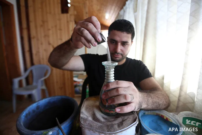 A Palestinian artist Khaled Salama, 27, paints on glass pots using colored sand, at his work shop in the West Bank city of Salfit, on Sep. 27, 2016. Photo by Shadi Hatem