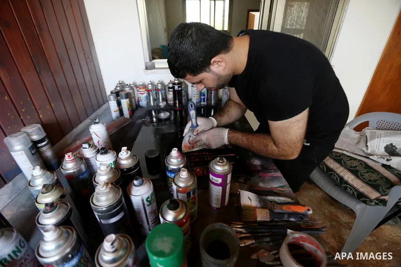 A Palestinian artist Khaled Salama, 27, paints on glass pots using colored sand, at his work shop in the West Bank city of Salfit, on Sep. 27, 2016. Photo by Shadi Hatem