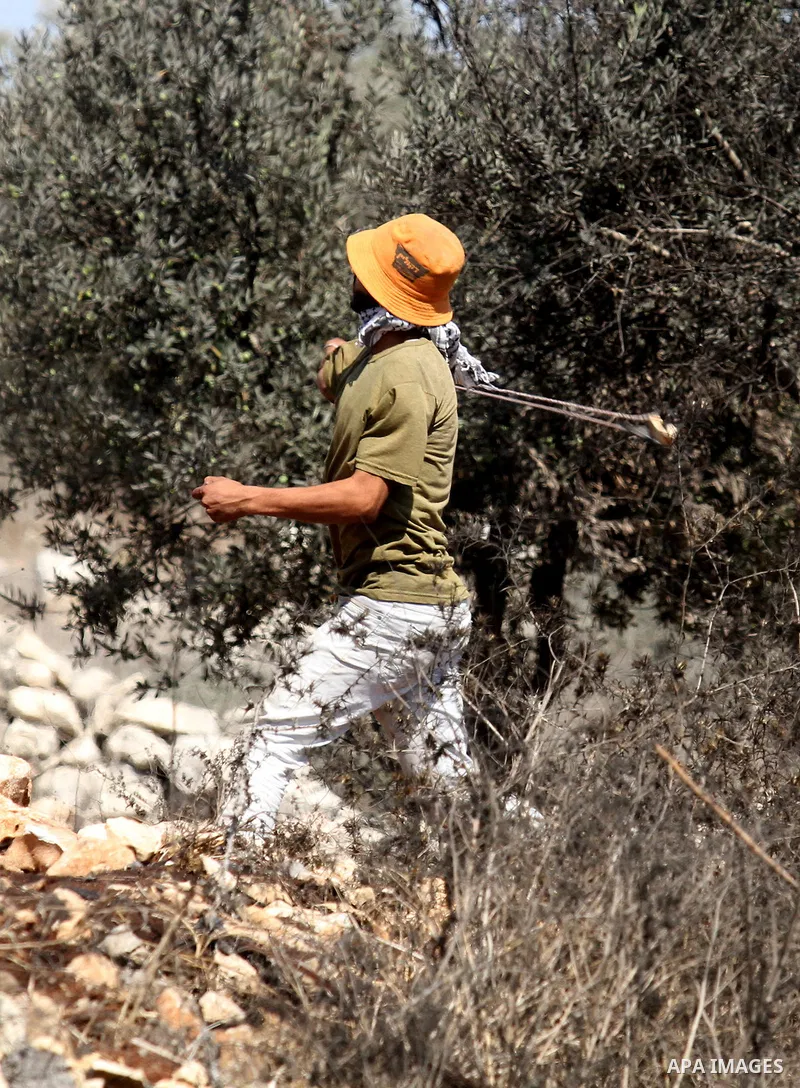 A Palestinian protester uses a slingshot to hurl stones toward Israeli security forces during clashes following a weekly demonstration against the expropriation of Palestinian land by Israel on Sep. 30, 2016, in the vill...