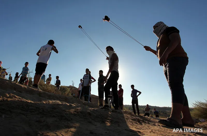 Palestinian protesters use a slingshot to hurl stones toward Israeli security forces during clashes near the border between Israel and Central Gaza Strip east of Bureij on Sep. 30, 2016. Photo by Ashraf Amra