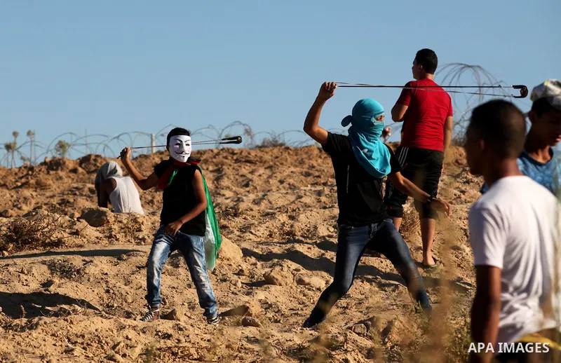 Palestinian protesters use a slingshot to hurl stones toward Israeli security forces during clashes near the border between Israel and Central Gaza Strip east of Bureij on Sep. 30, 2016. Photo by Ashraf Amra