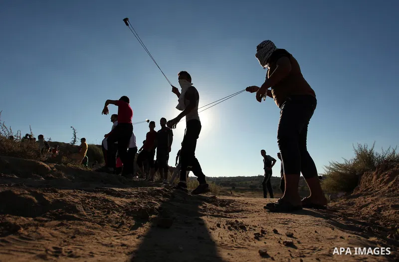 Palestinian protesters use a slingshot to hurl stones toward Israeli security forces during clashes near the border between Israel and Central Gaza Strip east of Bureij on Sep. 30, 2016. Photo by Ashraf Amra