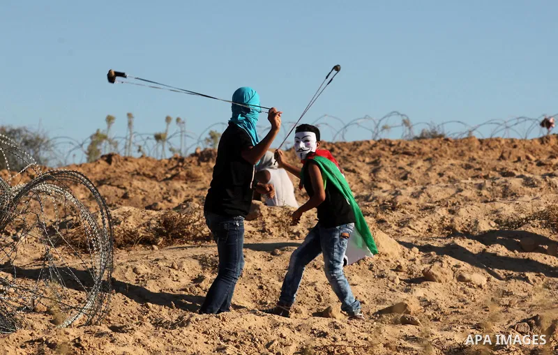 Palestinian protesters use a slingshot to hurl stones toward Israeli security forces during clashes near the border between Israel and Central Gaza Strip east of Bureij on Sep. 30, 2016. Photo by Ashraf Amra