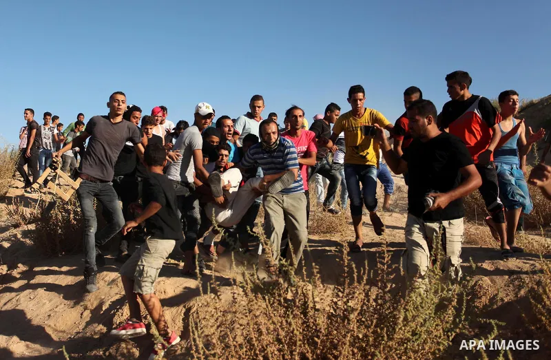 Palestinian protesters carry a wounded comrade during clashes with Israeli security forces near the border between Israel and Central Gaza Strip east of Bureij on Sep. 30, 2016. Photo by Ashraf Amra