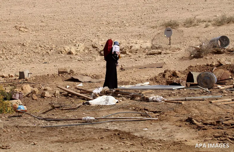A Palestinian woman carries a child as she inspects the remains of a house after it was demolished by Israeli authorities who said it was built without municipal permission on October 9, 2016 in the West Bank village of...