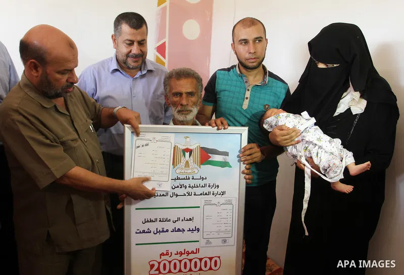 Members of the Interior Ministry in Gaza offer a certificate to Jihad and Tahany Shaath marking the birth of their son Waleed who is the two millionth baby to be born in Gaza at their house in the southern Gaza Strip tow...
