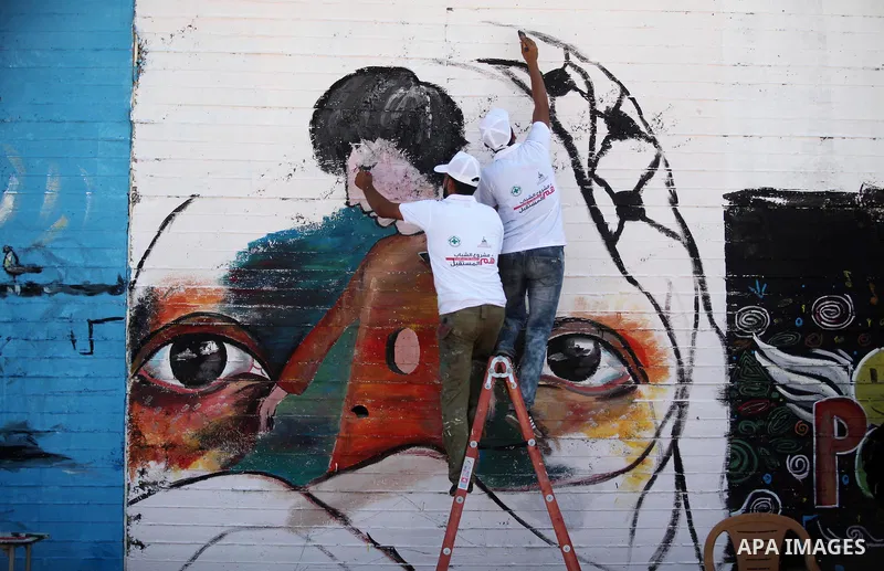 Palestinian artists paint a mural during a rally marking World Peace Day, in the port of Gaza city, on October 13, 2016. Photo by Ashraf Amra