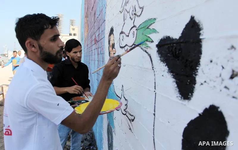 Palestinian artists paint a mural during a rally marking World Peace Day, in the port of Gaza city, on October 13, 2016. Photo by Ashraf Amra