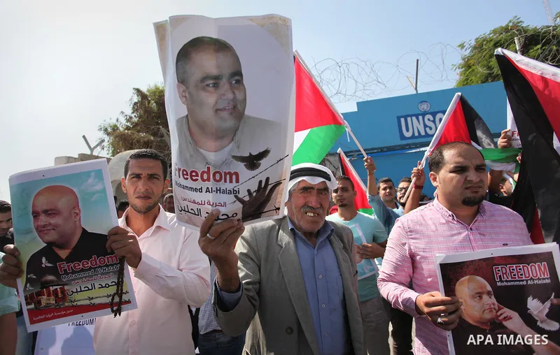 Palestinians hold posters of Mohammad El Halabi, World Vision's manager of operations in Gaza who was accused by Israel of funnelling millions of dollars in aid money to Hamas, during a protest in solidarity with El Hala...