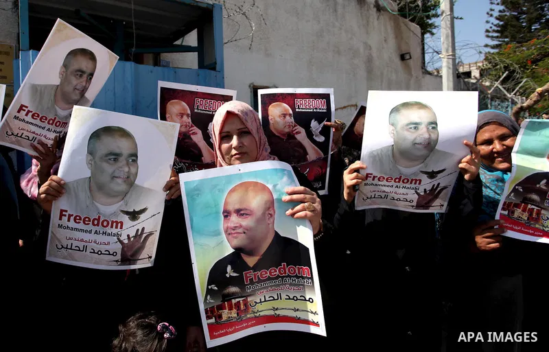 Palestinians hold posters of Mohammad El Halabi, World Vision's manager of operations in Gaza who was accused by Israel of funnelling millions of dollars in aid money to Hamas, during a protest in solidarity with El Hala...