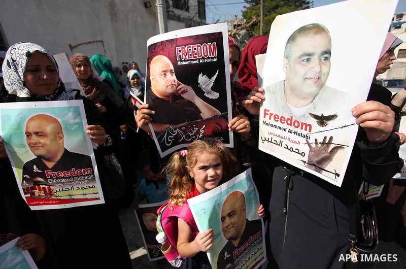 Palestinians hold posters of Mohammad El Halabi, World Vision's manager of operations in Gaza who was accused by Israel of funnelling millions of dollars in aid money to Hamas, during a protest in solidarity with El Hala...