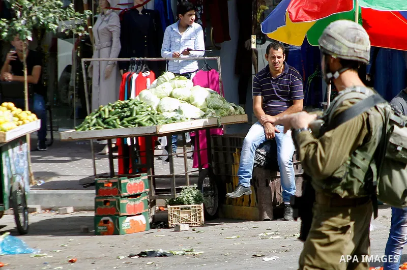 A member of Israeli security forces stands guard as Israeli settlers walk to visit the Jewish shrine of Atnaeil Ben Kinaz during the Jewish Sukkot holiday or the feast of the Tabernacles in a Palestinian neighbourhood of...