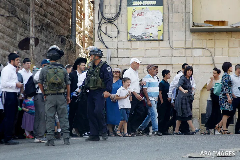 Israeli soldiers stand guard as Israeli settlers walk to visit the Jewish shrine of Atnaeil Ben Kinaz during the Jewish Sukkot holiday or the feast of the Tabernacles in a Palestinian neighbourhood of the divided West Ba...
