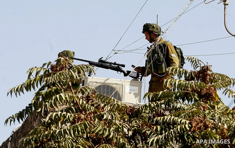 A member of Israeli security forces stands guard as Israeli settlers walk to visit the Jewish shrine of Atnaeil Ben Kinaz during the Jewish Sukkot holiday or the feast of the Tabernacles in a Palestinian neighbourhood of...