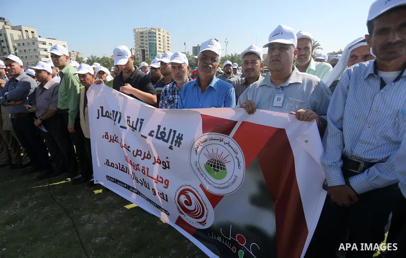 Palestinians hold banners during a protest against the United Nations mechanism for reconstruction and the Israeli blockade of the Gaza Strip, in Gaza City, on October 29, 2016. Photo by Mohammed Asad