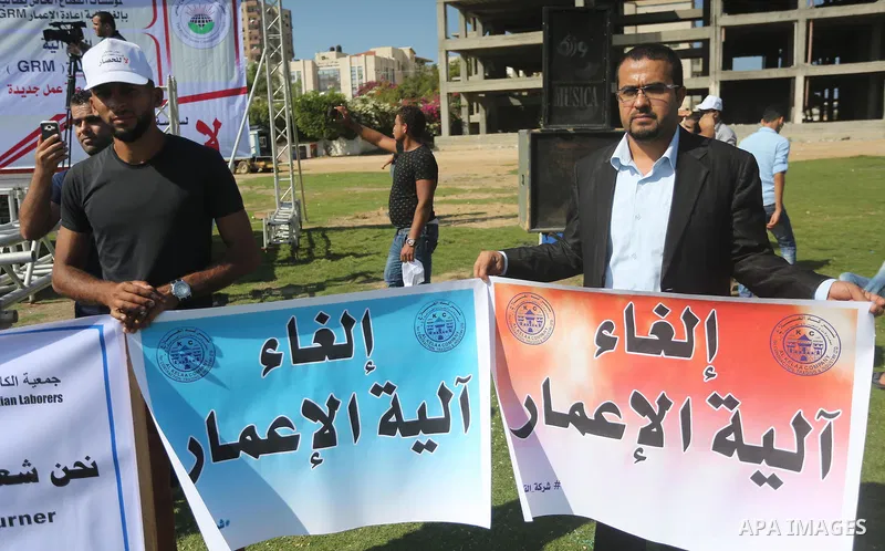 Palestinians hold banners during a protest against the United Nations mechanism for reconstruction and the Israeli blockade of the Gaza Strip, in Gaza City, on October 29, 2016. Photo by Mohammed Asad