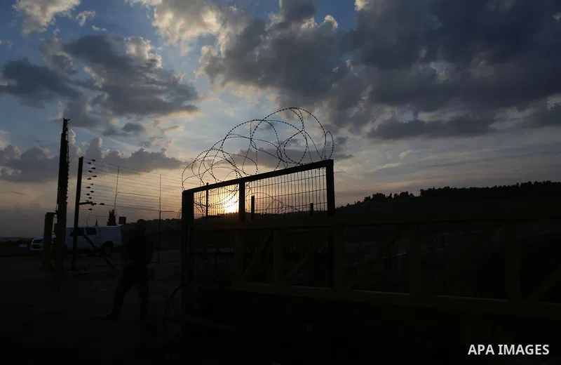 An Israeli soldier stands guard as Palestinians make their way to harvest olive trees during harvest season near the Israeli controversial separation wall in the village of Biddu, north west of Jerusalem, on October 31,...