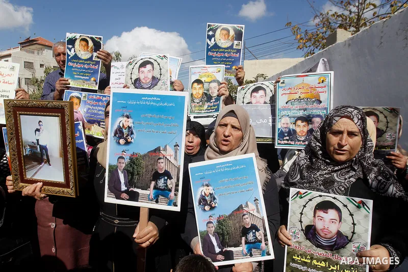 Palestinians hold banners during a protest to show solidarity with Palestinian prisoners in Israeli jails, in front of Red cross office in the West Bank city of Hebron, on October 31, 2016. Photo by Wisam Hashlamoun