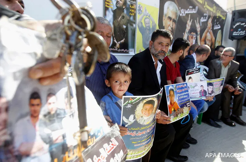 Palestinians hold banners during a protest to show solidarity with Palestinian prisoners in Israeli jails, in front of Red cross office in the West Bank city of Hebron, on October 31, 2016. Photo by Wisam Hashlamoun