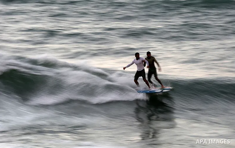 Palestinian men surf off the beach of Gaza City on November 2, 2016. Photo by Yasser Qudih